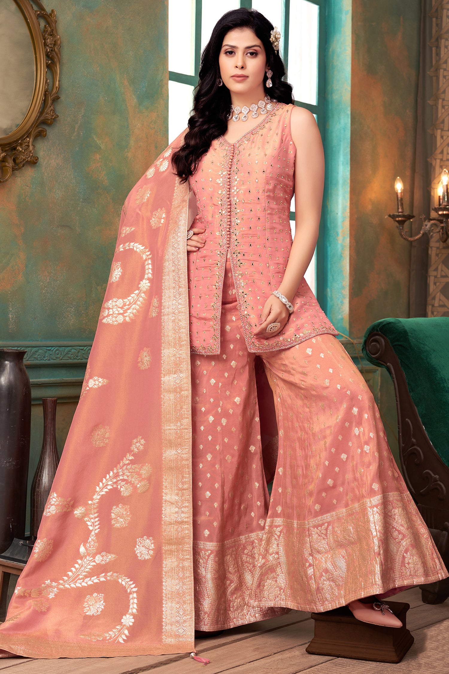 Woman in a peach traditional outfit with a matching dupatta in a decorated room.
