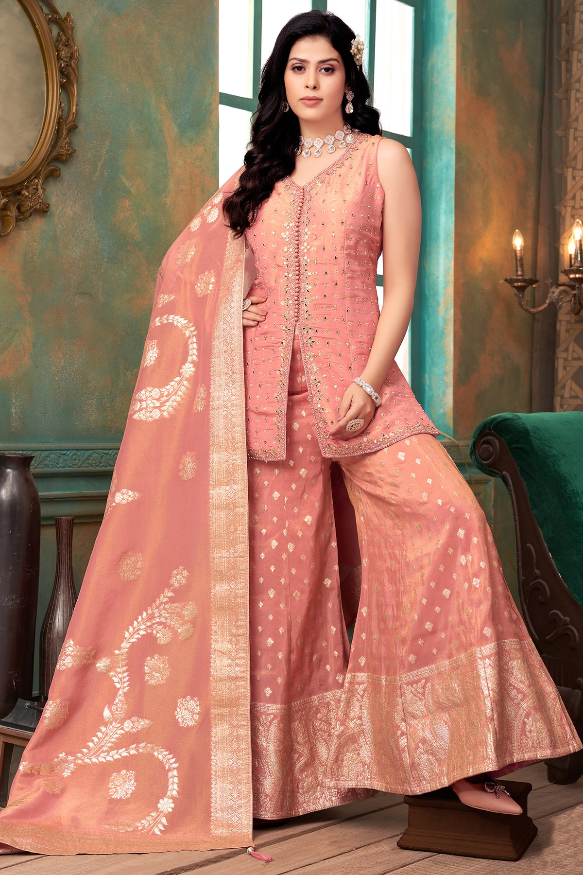 Woman in a peach traditional outfit with a matching dupatta in a decorated room.